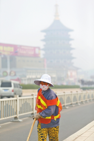 近日，在古都洛陽(yáng)，環(huán)衛(wèi)工人身后的“天堂”被霧霾籠罩著。