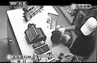 戴帽男子一手掐住加油站營業(yè)員，一手持發(fā)令槍指向另一營業(yè)員，要求“把錢給我裝起來”。