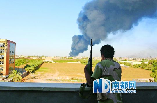 2日，利比亞首都的黎波里，一民兵武裝成員眺望被火箭彈擊中的儲(chǔ)油罐冒出濃煙。