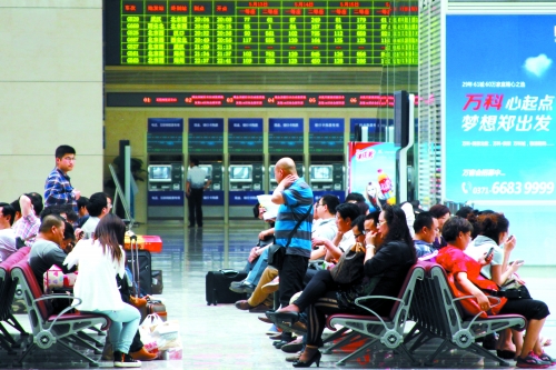 候車大廳溫度很高，一名乘客一手扇風(fēng)、一手擦汗