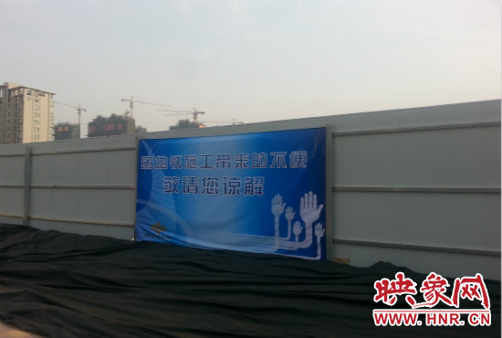 道路南側(cè)圍起了白色的圍擋，墻上標(biāo)示著“因地鐵施工帶來的不便敬請(qǐng)您諒解”的提示牌。