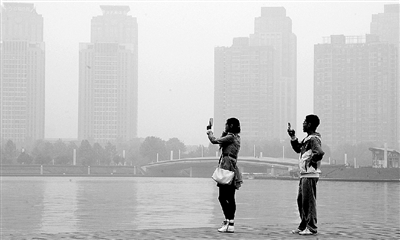 29日中午，鄭東新區(qū)如意湖畔，兩個(gè)年輕人拍攝霧霾中的景色。 鄭州晚報(bào)記者 馬健 圖