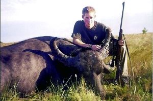 哈里王子手持獵槍，蹲在一頭遭到獵殺的水牛旁邊