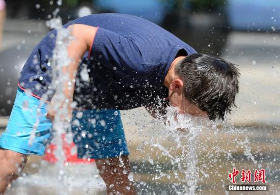 5月29日，一名小孩將頭伸向北京街頭的噴泉以降溫祛暑。