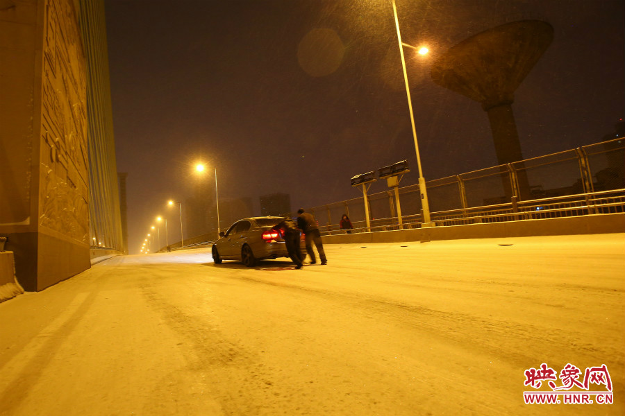 雪天路滑，汽車上橋打滑，兩名“推車人”幫助一輛私家車上坡。