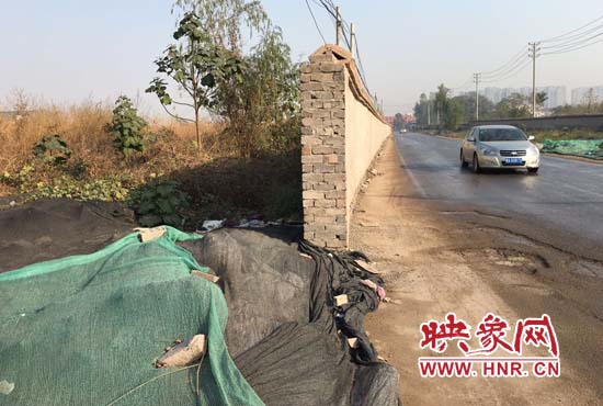 一墻之隔，一邊是道路，一邊是垃圾和荒草，市民質(zhì)疑其為遮羞墻。