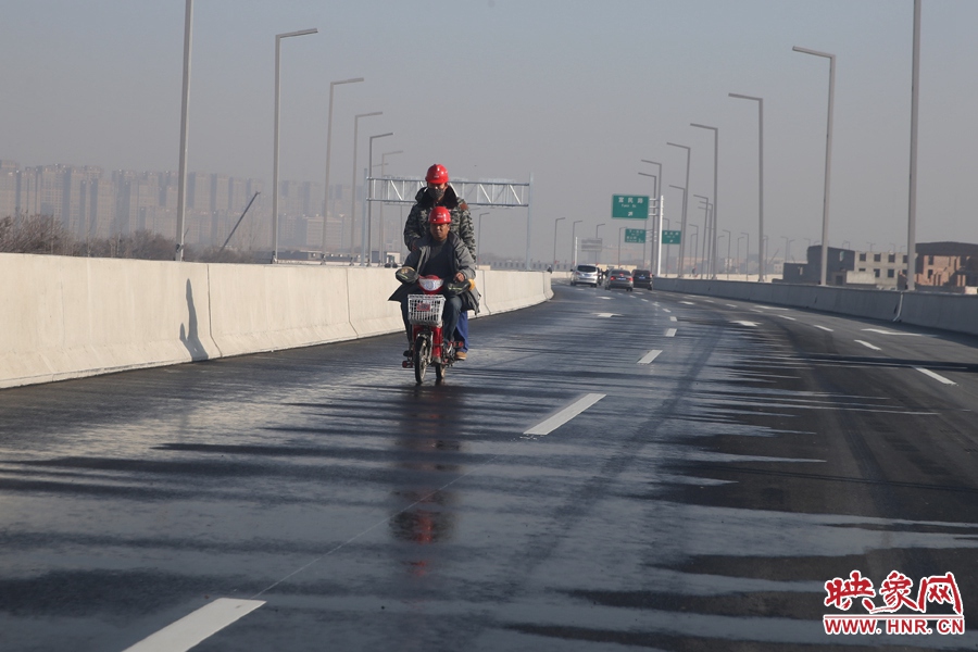 兩名工人騎車經(jīng)過灑水養(yǎng)護(hù)路面。