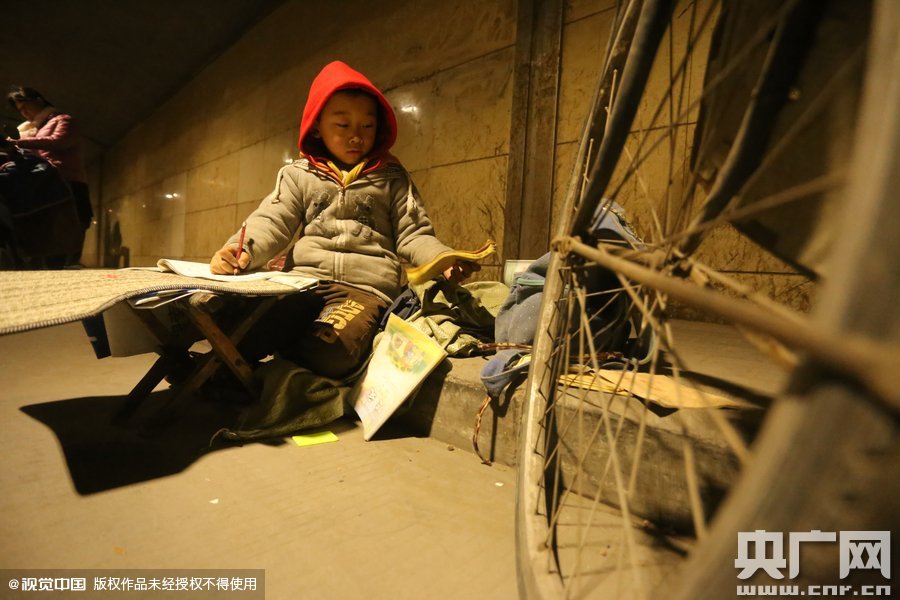 2015年11月8日晚，鄭州，7歲男孩涵洞橋下陪父母練攤，路邊燈下坐小馬扎上寫(xiě)作業(yè)。
