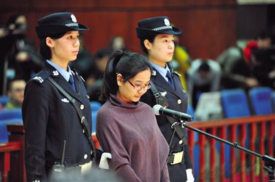 被告人盧梅低著頭，站在朝陽法院刑事審判庭的被告席上。